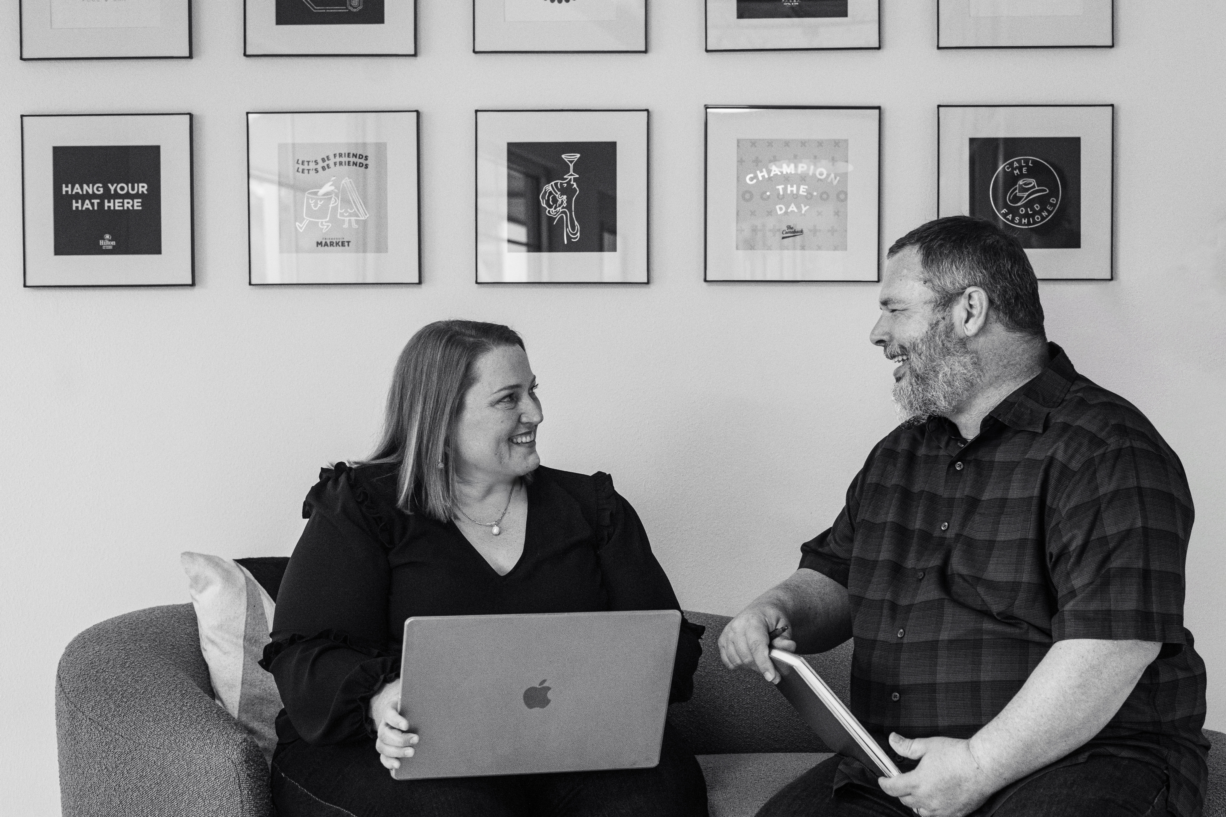 Business Duos A husband-and-wife business team sits together on a couch, one using a laptop and the other with a tablet, engaged in an animated discussion about their next joint venture. The scene captures the energy of married couples in business, entrepreneur couples collaborating on new ideas, and partners navigating both marriage and business in a stylish home office space decorated with framed art—perfect inspiration for couple-run businesses or anyone seeking business advice for married couples working together.